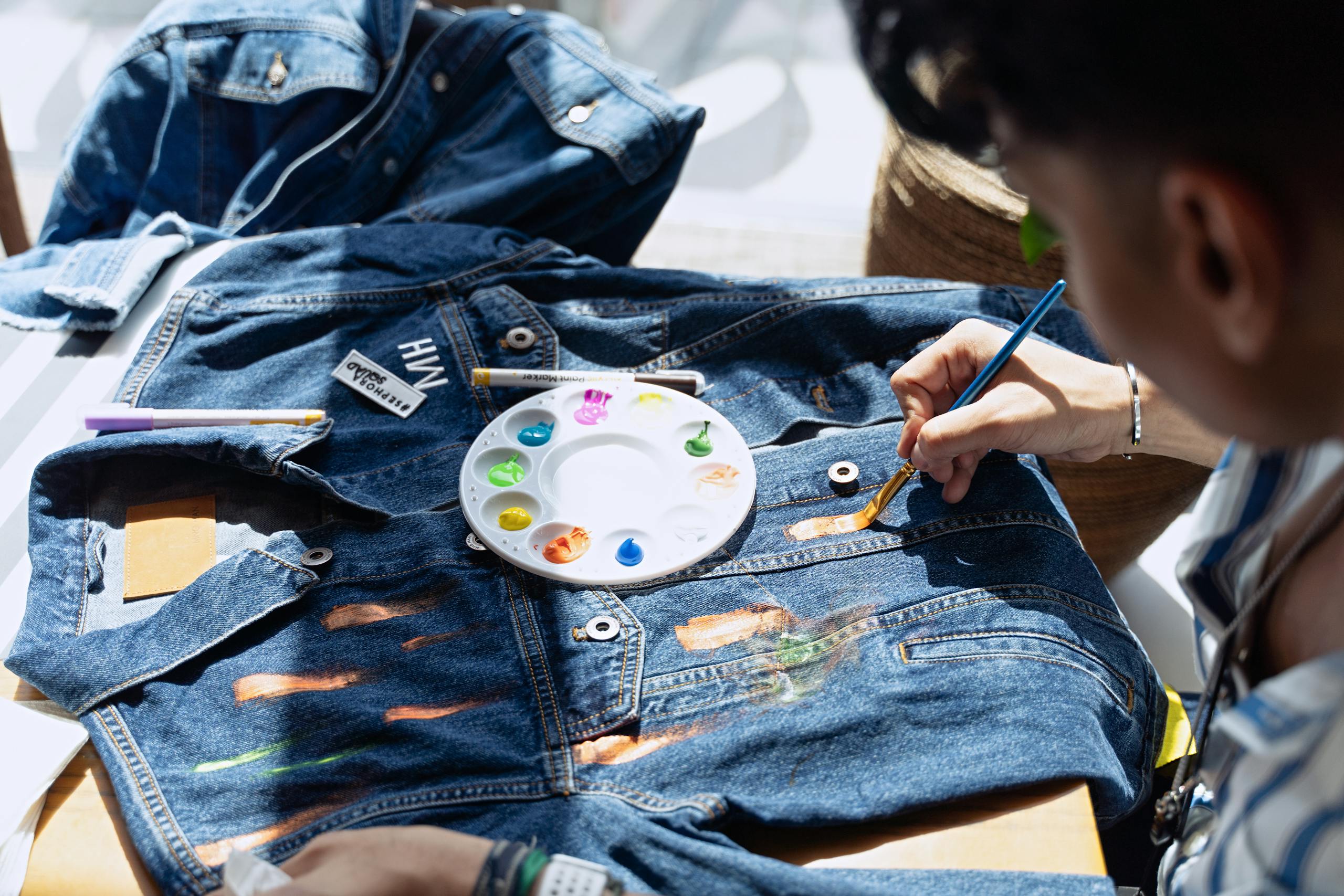 Artist painting denim jacket with vibrant colors in a bright Dubai studio.